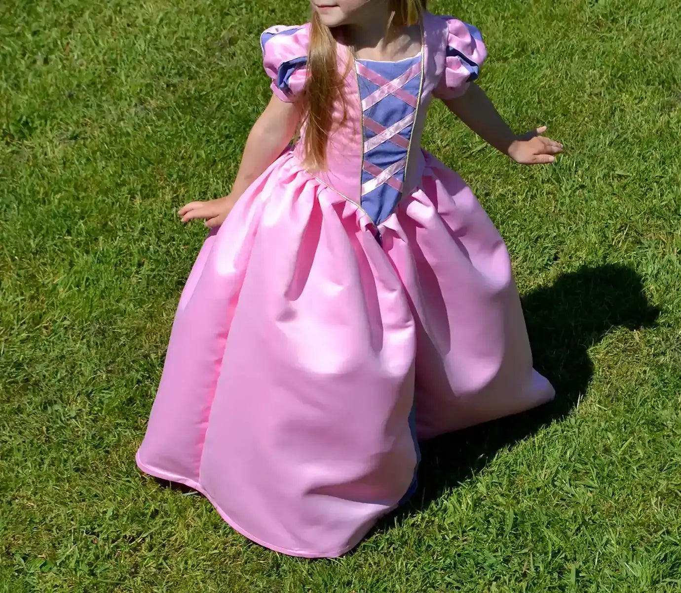 Petite fille en robe rose de princesse inspirée de Raiponce, manches ballon et rubans croisés, debout dans l’herbe - patron de couture Margaux de Kandix