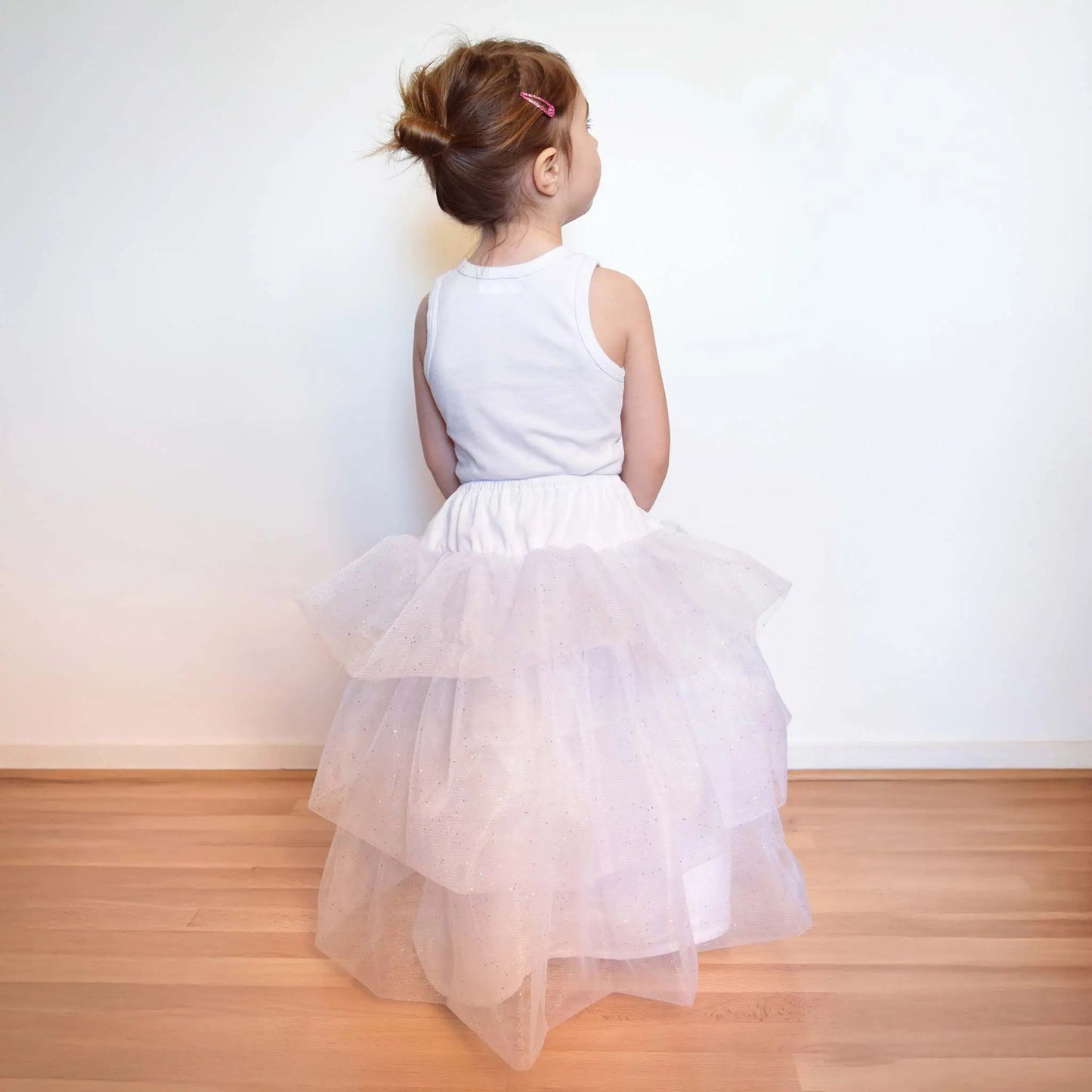 Petite fille en jupon blanc à volants de tulle, vue de dos avec un chignon et une barrette rose – patron de couture Kandix