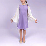 Fillette souriante de face dans une robe lilas avec manches longues blanches fluides, bras relâchés - patron de couture Gaby de Kandix