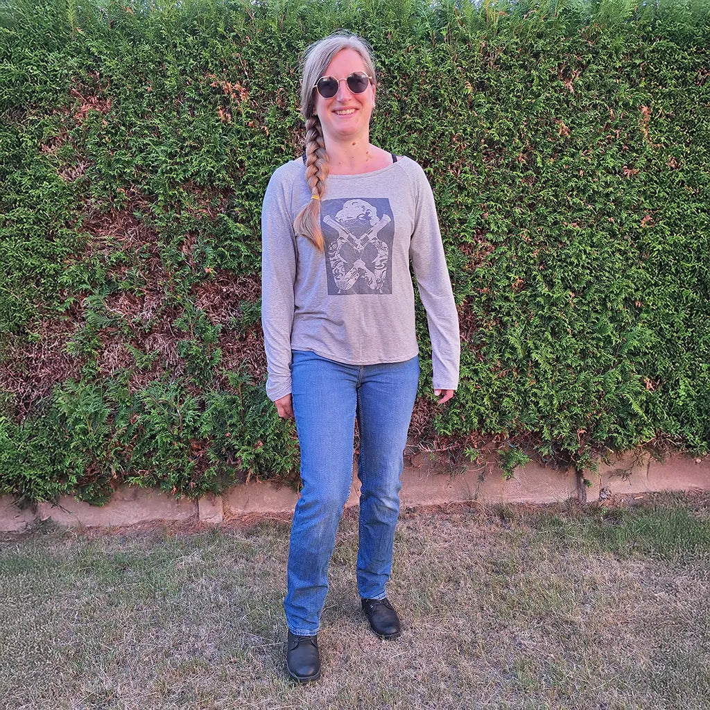 T-shirt raglan femme gris clair uni à manches longues, imprimé graphique sur le devant, porté avec un jean devant une haie – patron de couture Tao de Kandix