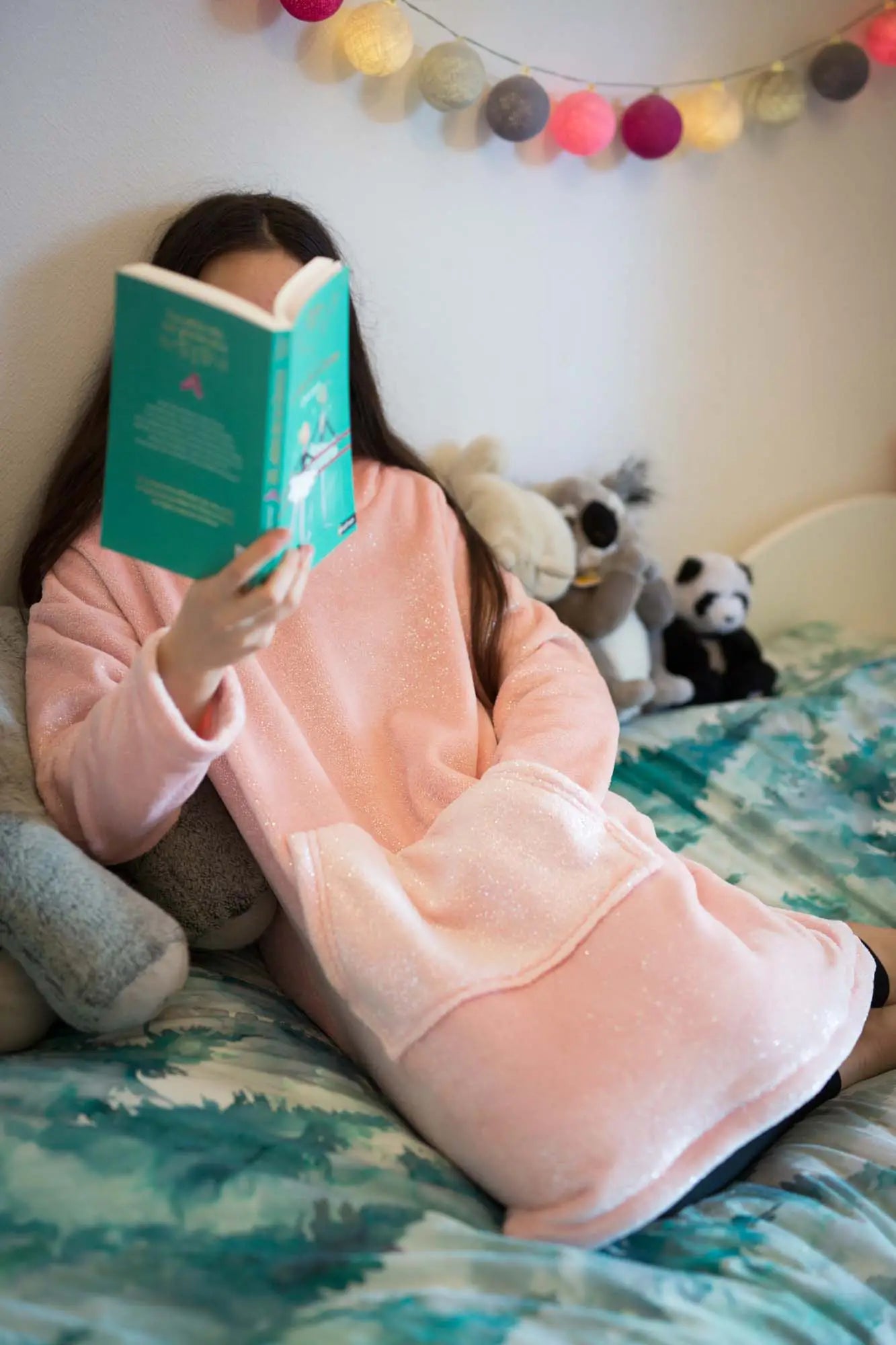 Adolescente en sweat doudou Casimir rose pailleté, assise sur un lit, en train de lire - patron de couture Kandix