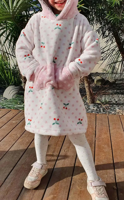 Sweat doudou enfant blanc à pois roses et motifs cerises, capuche relevée, mains dans la poche kangourou, en extérieur sur terrasse boisée - patron de couture Casimir de Kandix