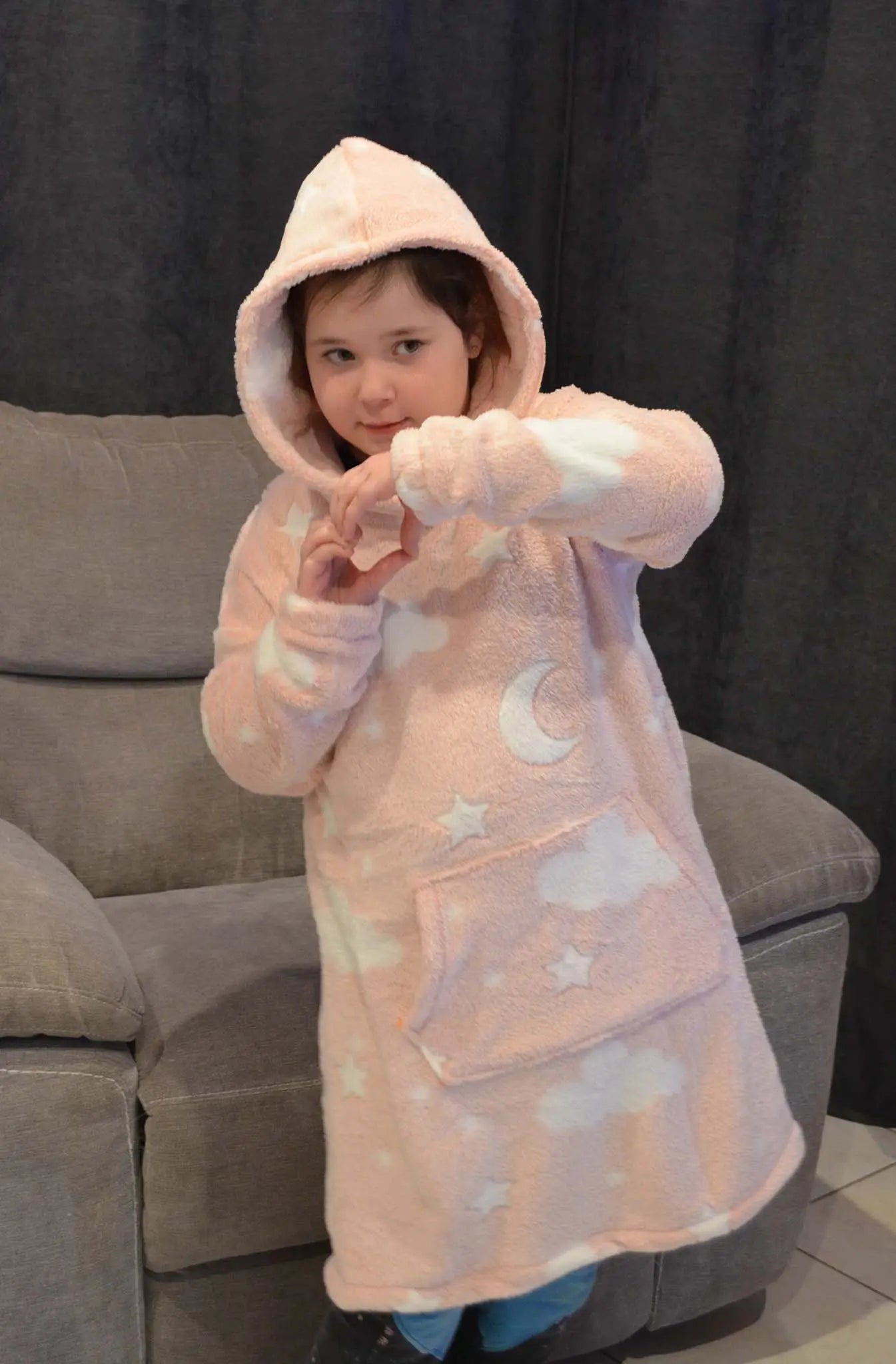 Enfant portant un sweat doudou rose à capuche imprimé étoiles et nuages, debout devant un canapé en formant un cœur avec les mains - patron de couture Casimir de Kandix