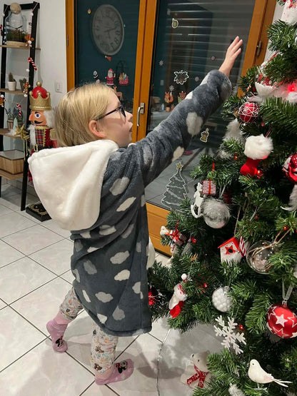 Enfant de profil habillée d’un sweat doudou gris à capuche crème et motifs nuages, levant la main pour décorer un sapin de Noël - patron de couture Casimir de Kandix