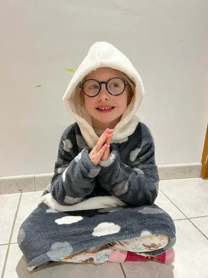 Enfant souriante assise au sol en tailleur, vêtue d’un sweat doudou à capuche imprimé nuages, mains jointes devant elle - patron de couture Casimir de Kandix