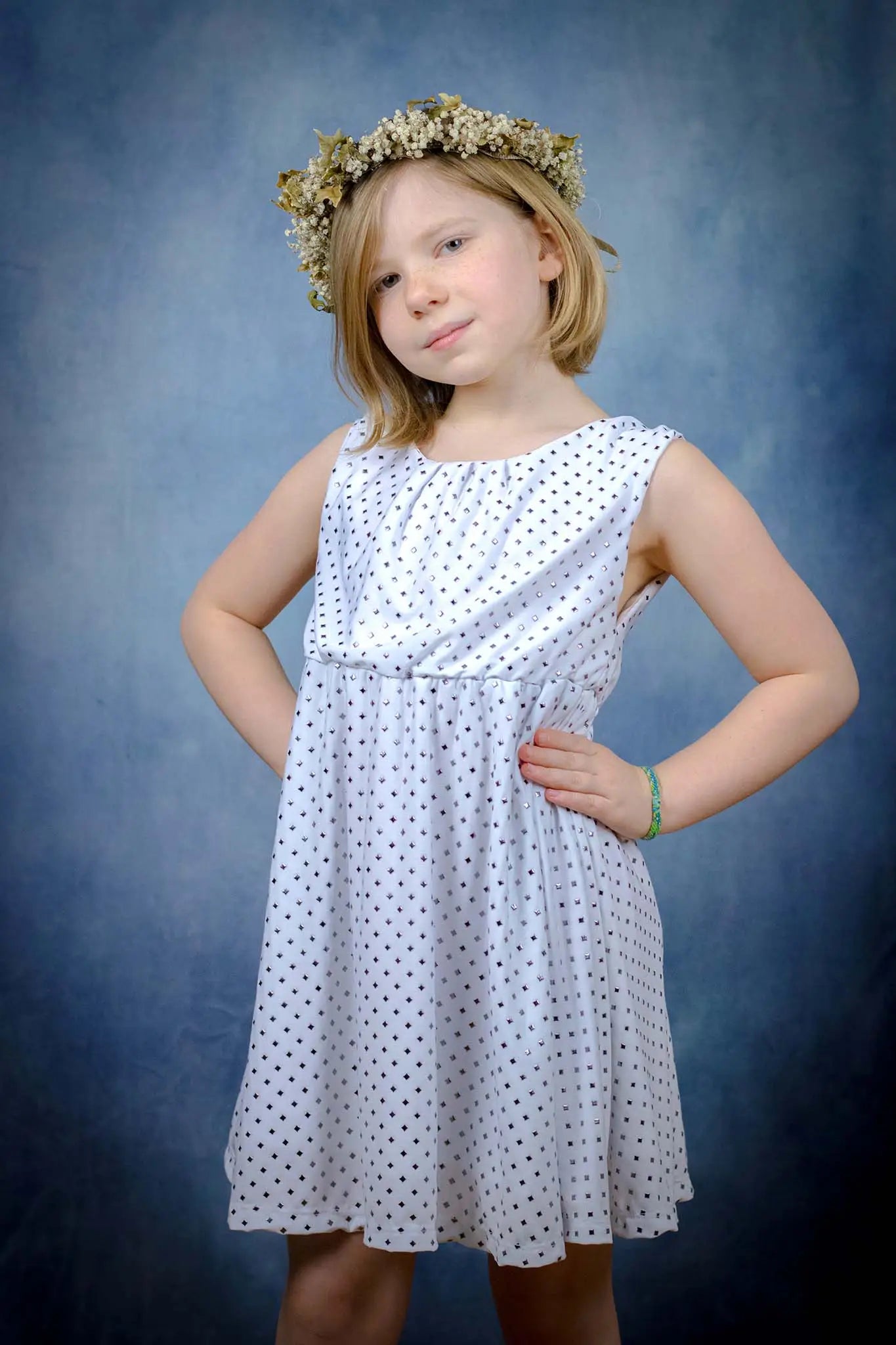 Robe blanche enfant en tissu à sequins, vue de face avec les mains sur les hanches, fond bleu studio - patron de couture Cylia de Kandix