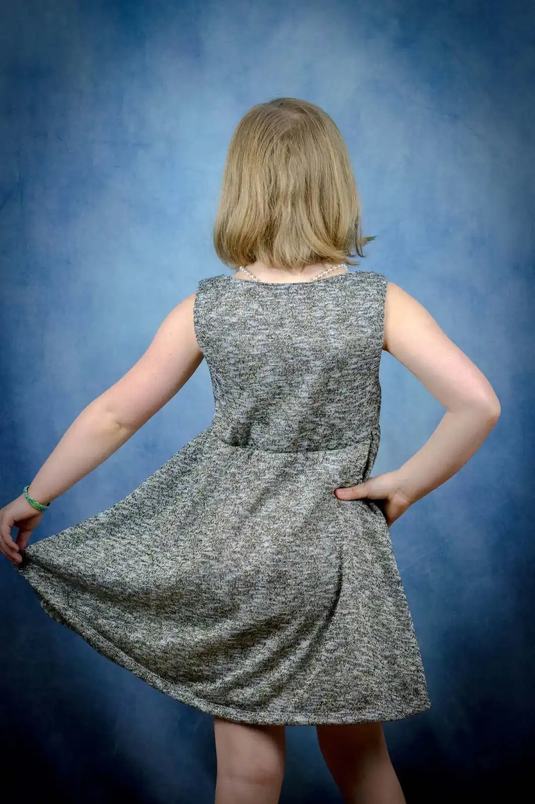 Vue de dos de la robe enfant en maille pailletée grise, jupe tenue dans la main – patron de couture Cylia de Kandix