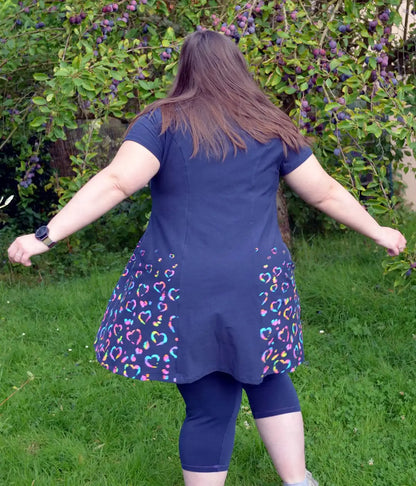 Vue de dos d'une femme tournant sur l'herbe, en robe bleu marine décorée de cœurs multicolores, dans un jardin - patron de couture Gaby de Kandix