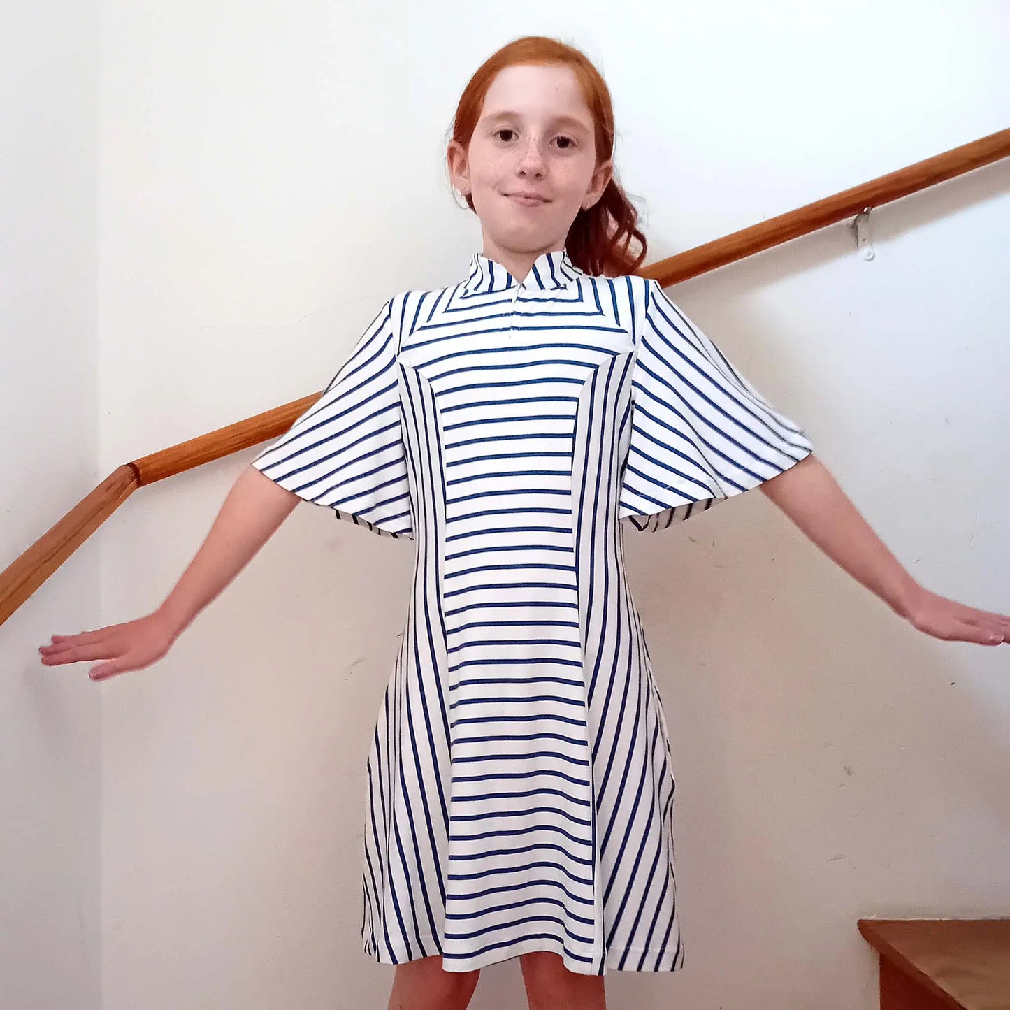 Petite fille en robe Gaby à rayures, bras ouverts et petit sourire joueur - patron de couture Kandix