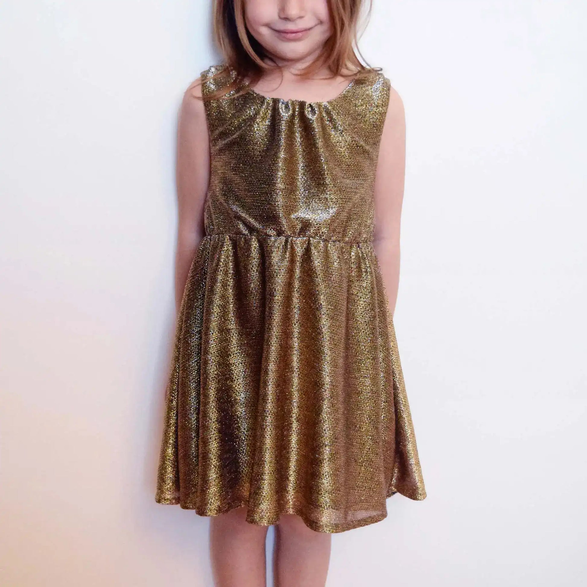 Robe enfant dorée en tissu lurex portée de face avec un léger sourire – patron de couture Cylia de Kandix