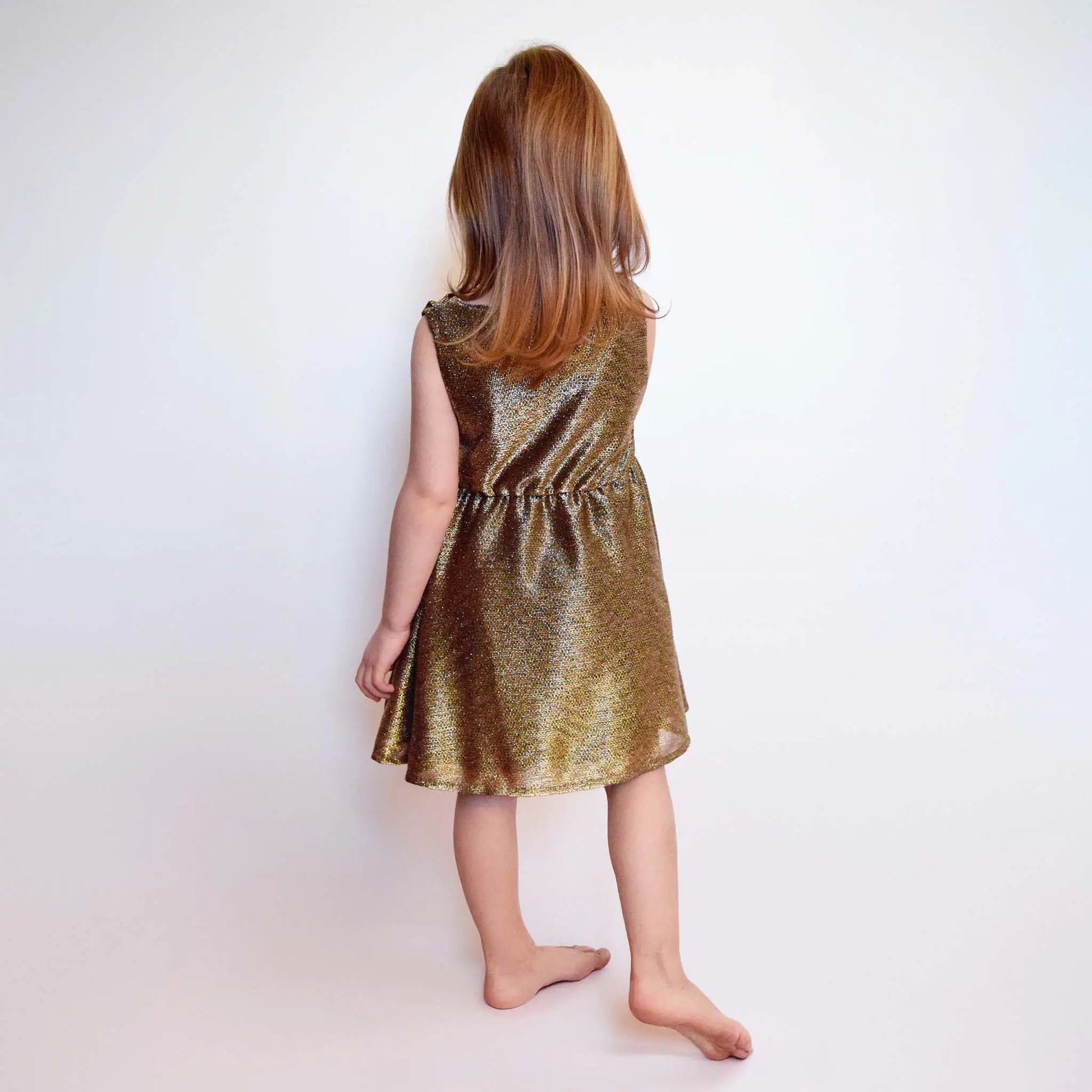 Fillette debout de dos en robe dorée lurex, cheveux lâchés – patron de couture Cylia de Kandix