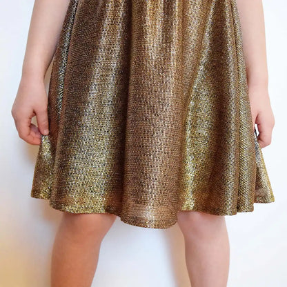 Zoom sur la jupe brillante d’une robe dorée tenue par la main d’une enfant – patron de couture Cylia de Kandix