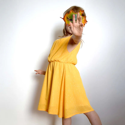 Robe enfant en jaune lumineux, pose dynamique avec main tendue et masque en feuille – patron de couture Cylia de Kandix