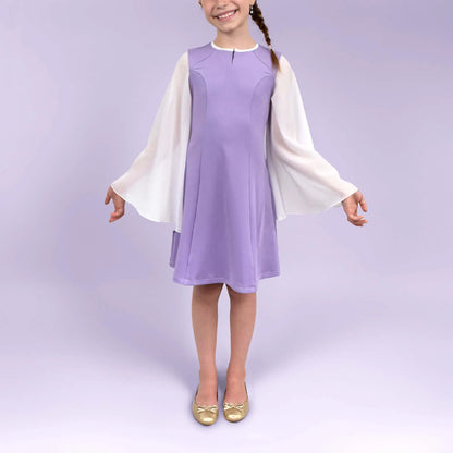 Fillette souriante de face dans une robe lilas avec manches longues blanches fluides, bras relâchés - patron de couture Gaby de Kandix