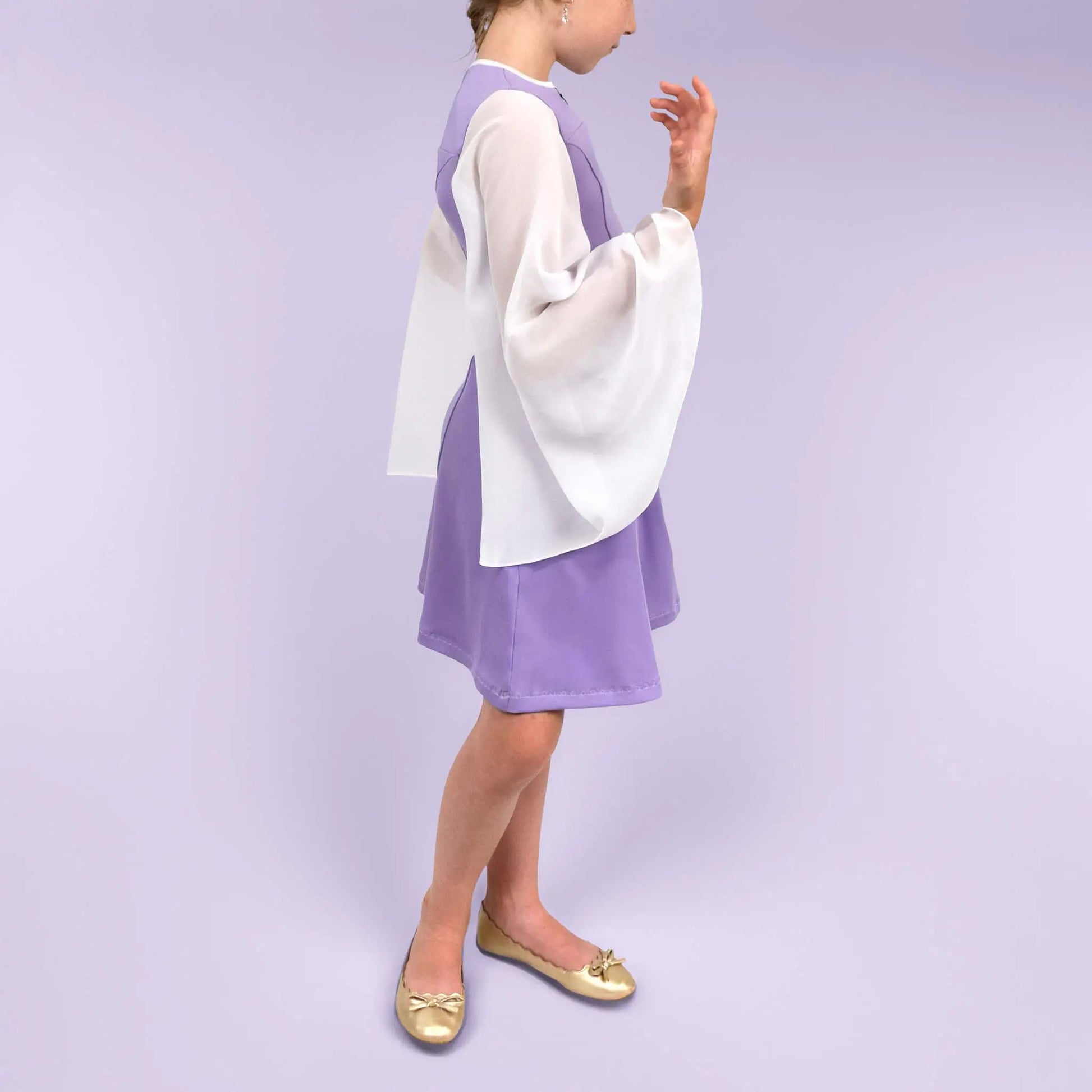 Vue de profil d’une fillette dans une robe lilas avec les manches en mousseline blanche, main levée vers le visage - patron de couture Gaby de Kandix