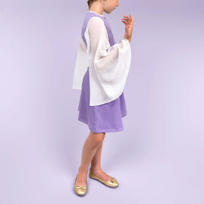 Vue de profil d’une fillette dans une robe lilas avec les manches en mousseline blanche, main levée vers le visage - patron de couture Gaby de Kandix