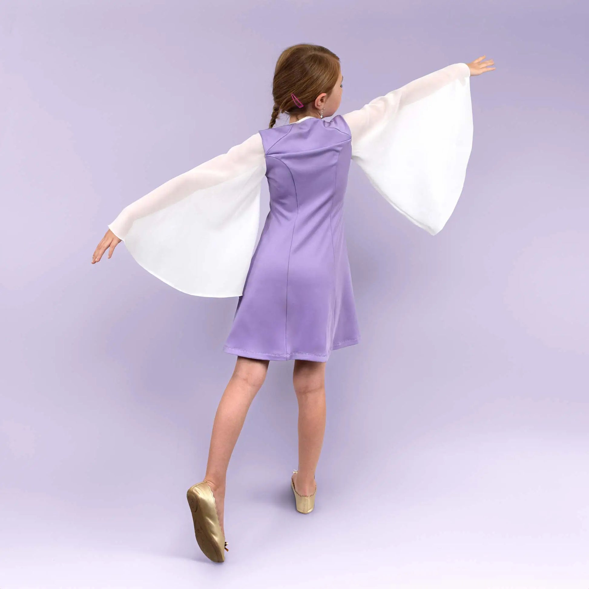 Petite fille de dos en mouvement, bras étendus comme des ailes, robe lilas et manches blanches amples - patron de couture Gaby de Kandix