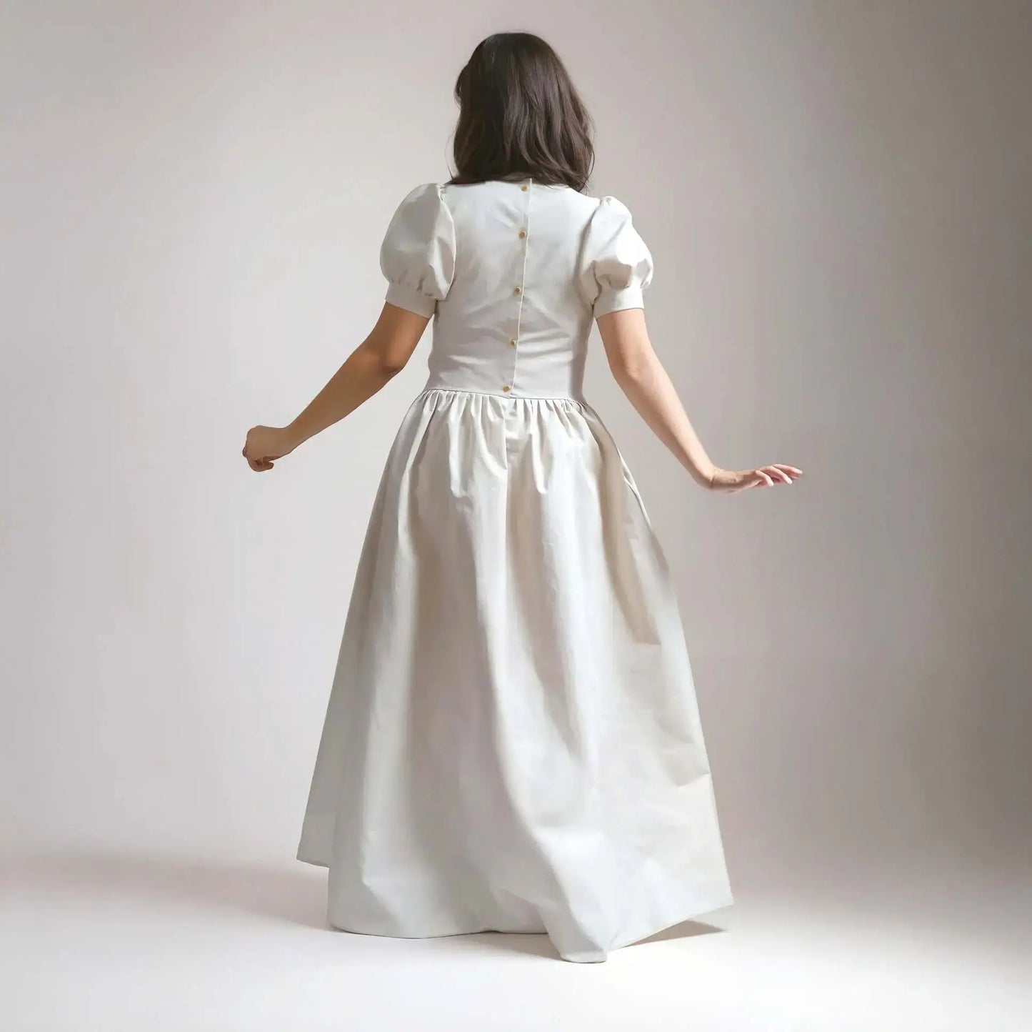 Robe princesse écrue vue de dos avec boutons contrastés, en mouvement dans un décor neutre – patron de couture Margaux de Kandix