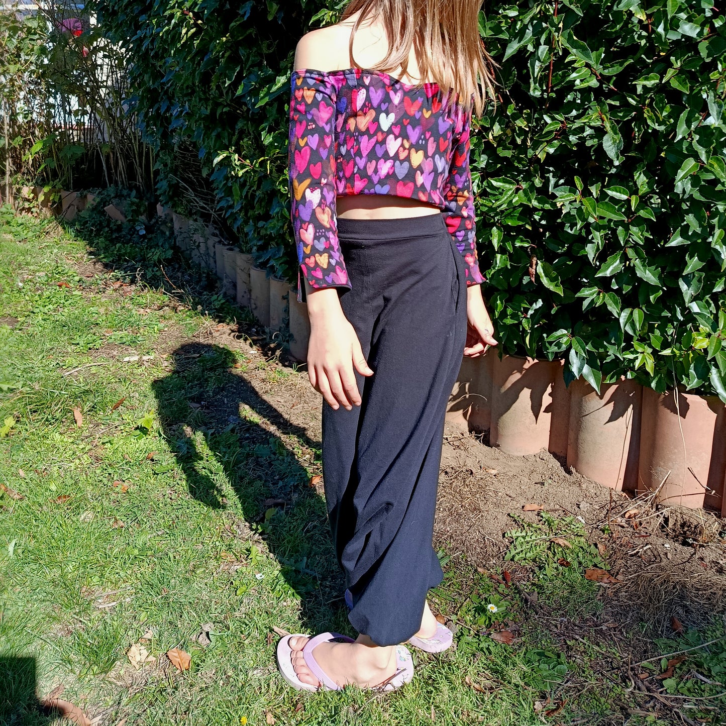 Top Yasmine enfant imprimé cœurs multicolore manches longues, porté avec pantalon noir, vue de profil en extérieur – patron Kandix