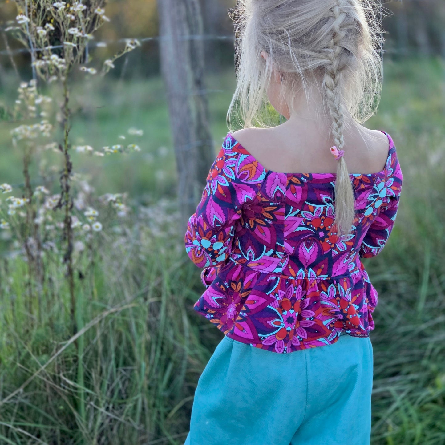 Top Yasmine enfant imprimé rose et violet manches longues, porté avec pantalon bleu, vue de dos en extérieur – patron Kandix