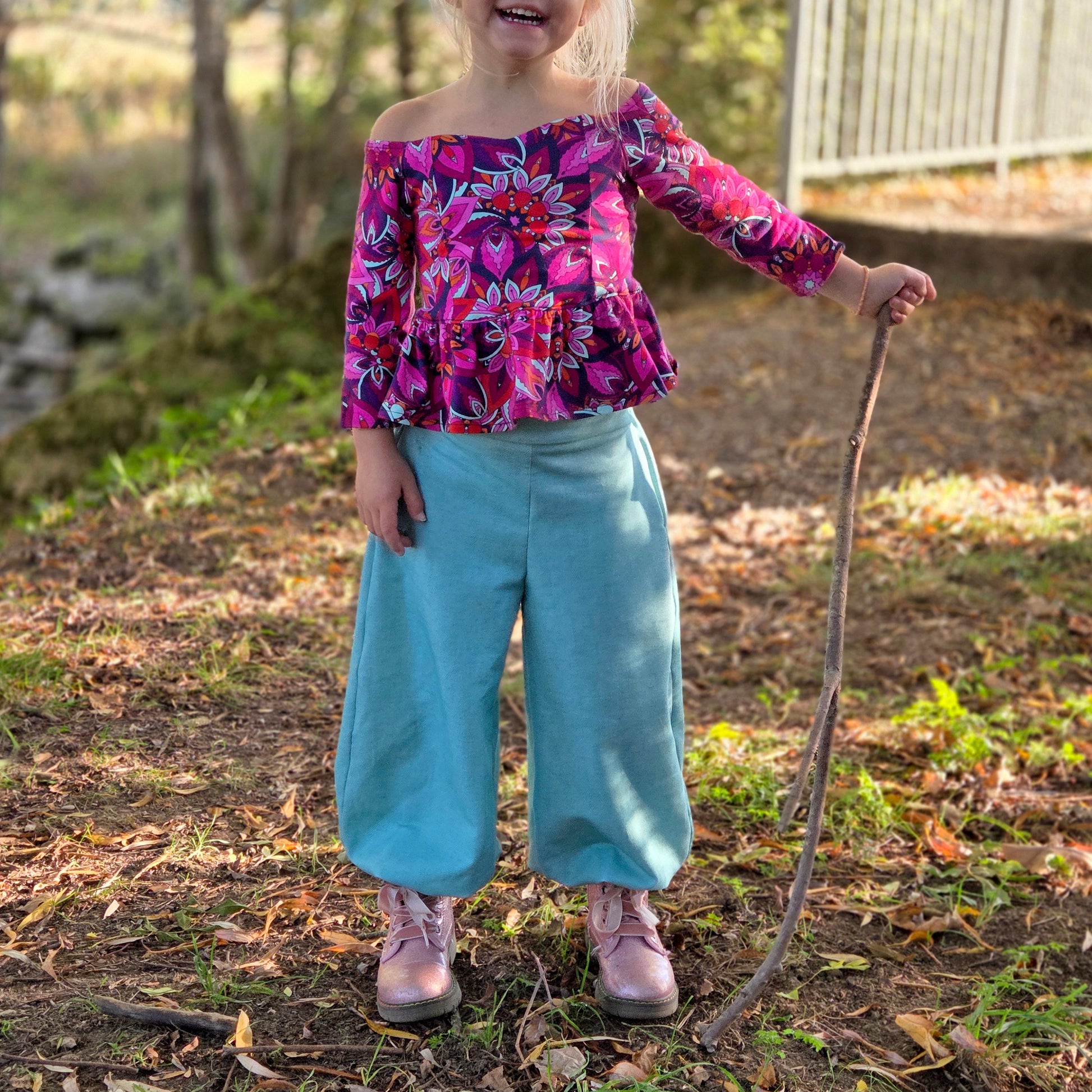 Top Yasmine enfant imprimé rose et violet manches longues, porté avec pantalon bleu large, vue de face en extérieur – patron Kandix